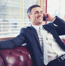 Smiling businessman sitting and talking on the phone at office